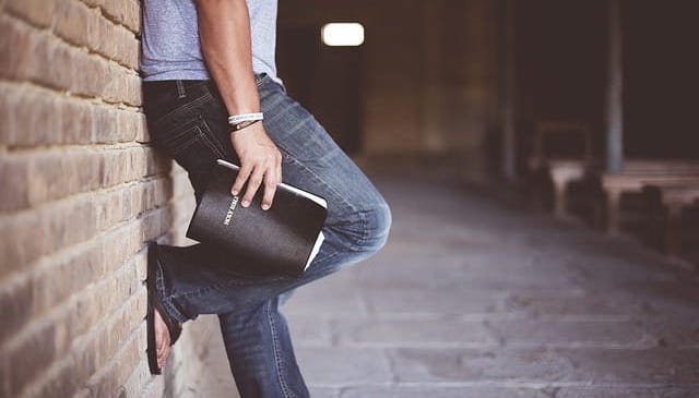 Ein Mann mit Bibel in der Hand steht an gelegt an einer Mauer