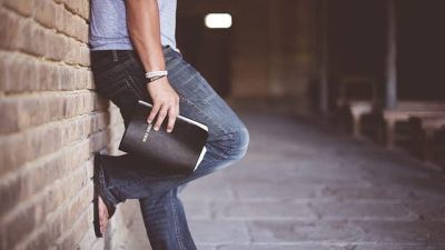 Ein Mann mit Bibel in der Hand steht an gelegt an einer Mauer